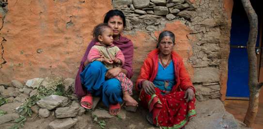 A grandmother, mother and child sit outside their collapsed home in India