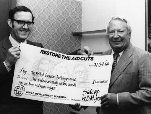 Politician Ted Heath presented with 'Restore the Aid Cuts' cheque for £230m from treasurer of World Development Movement group.
