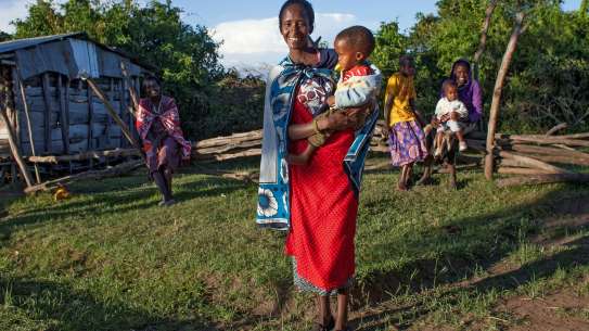 A mother stands in a Maasai village in Kenya, holding her child on her hip
