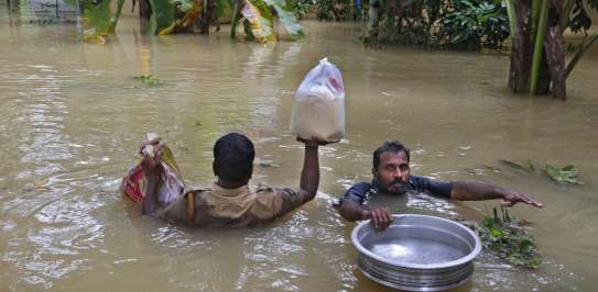 An Indian policeman, left, and a volunteer carry essential supplies for stranded people in a flooded area in Chengannur