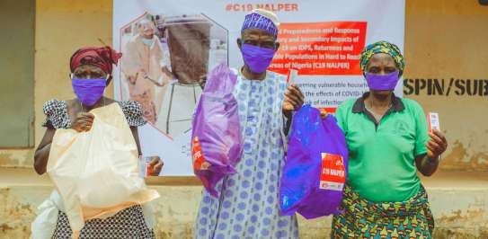 Three people wearing masks in Nigeria showing their bags of hygiene items they received from Christian Aid partners