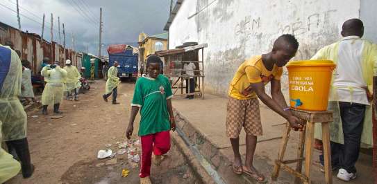 Boy in street in Sierra Leone washing his hands at wash station set up to control Ebola.