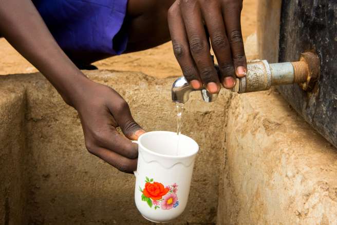 Hands of a primary school pupil filling a cup with water from a drinking water tap
