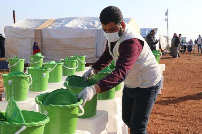 A masked partner field staff member prepares the hygiene kit items in green buckets for distribution