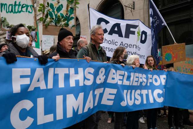 Protesters hold a long banner reading Faith and Belief for Climate Justice at COP26 Climate march
