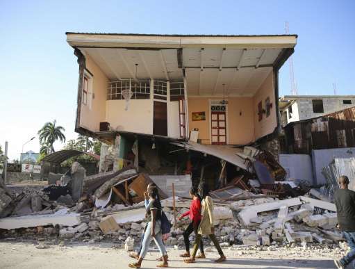 People walk past a home destroyed by the earthquake in Les Cayes, Haiti.