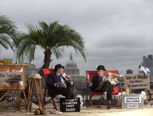 Two men in suits relaxing in sun loungers with a sign next to them saying "Isle of shady tax haven: poor people keep out!"