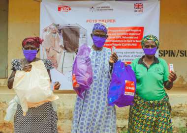Three people wearing masks in Nigeria showing their bags of hygiene items they received from Christian Aid partners