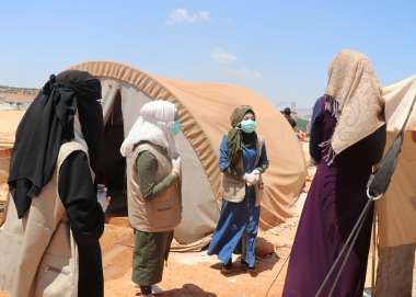 Three masked members of one of the Volunteer First Response Committees conduct awareness-raising in an IDP camp
