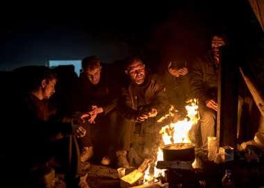 Five men sitting around a campfire in the dark.